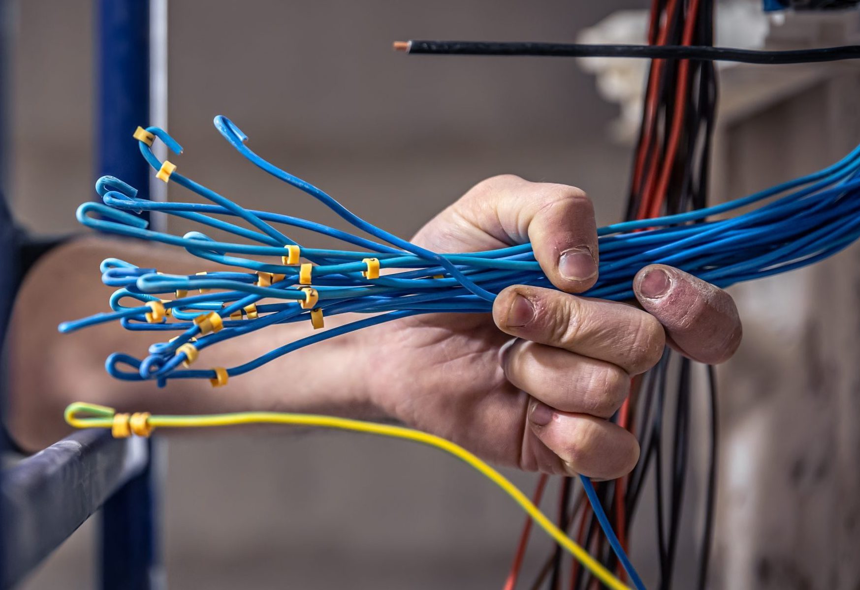 A male electrician works in a switchboard with an electrical connecting cable.